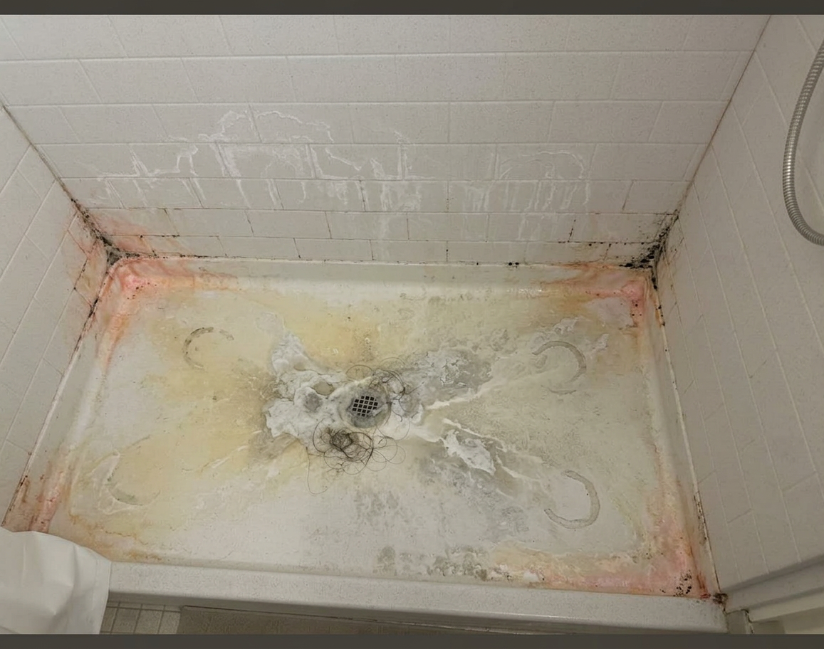 Walk-in shower floor with heavy rust stains, mold, hair, and grime buildup before restoration